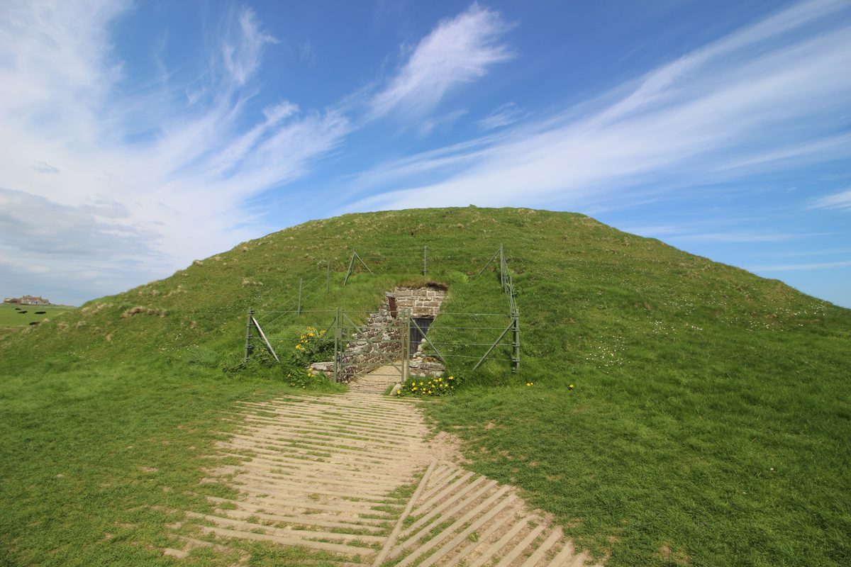 Maeshowe, a grass-covered mound in Orkney, under a pale sky